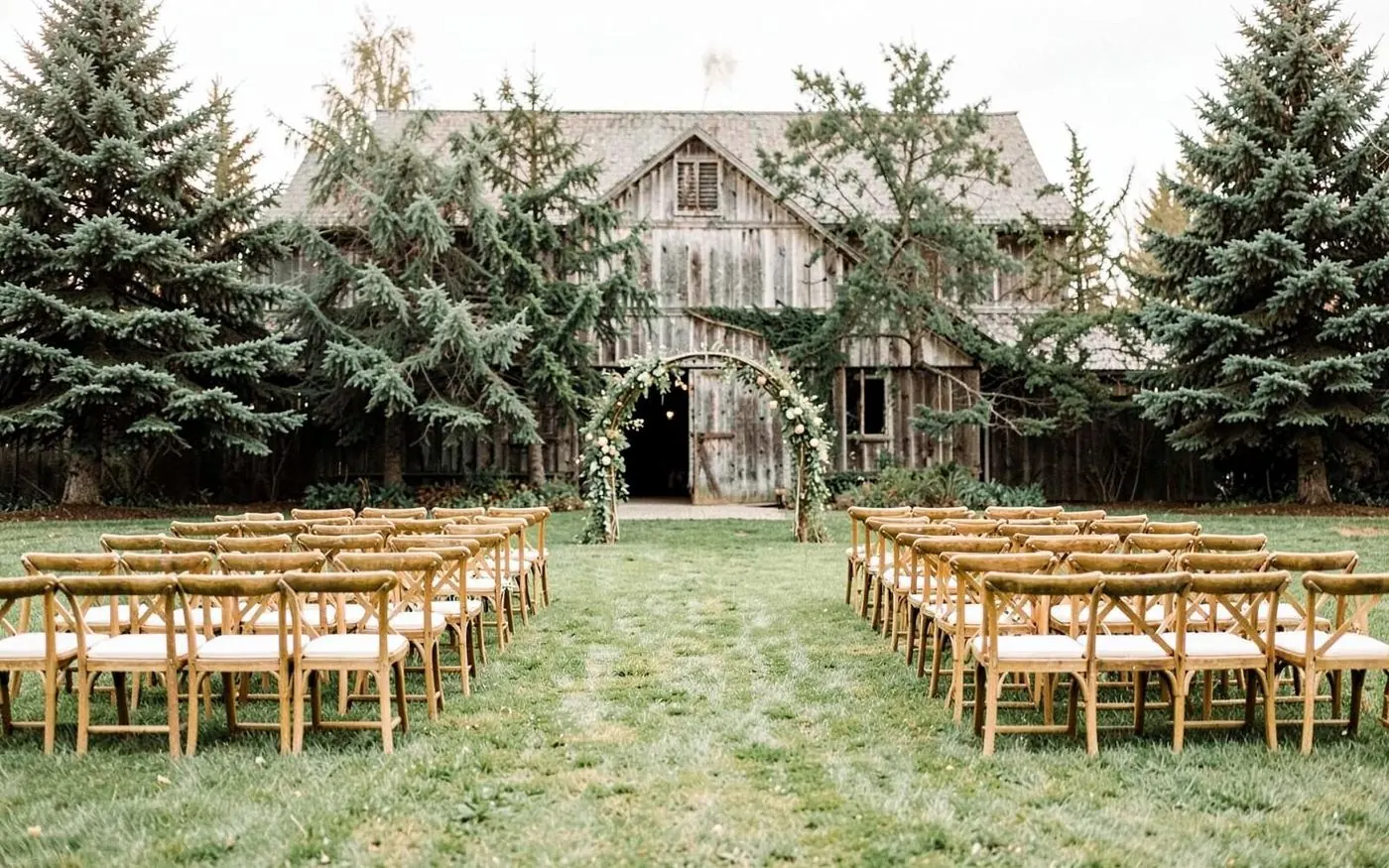 Barn venue lawn set with rows of wooden chairs for an outdoor ceremony